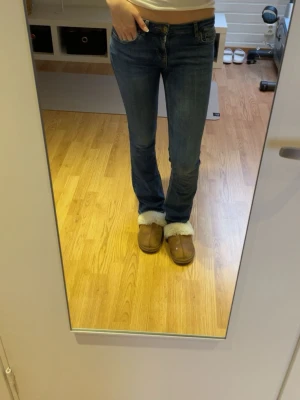 Blå bootcut jeans med låg midja - Säljer ett par klassiska blå bootcut jeans med låg midja. Jeansen har en smal passform upptill och lätt utsvängda ben. Perfekta till vardags och passar till det mesta. Materialet är mjukt denim i bomull.