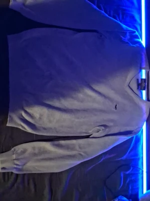 Ljusgrå tröja från Hampton Republic - Ljusgrå långärmad tröja från Hampton Republic med V-ringning och diskret logga broderad på bröstet. Tillverkad i högkvalitativ bomull för en mjuk och skön känsla. Perfekt för en clean och stilren look.