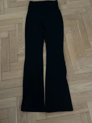 Svarta utsvängda träningsbyxor  - Snygga svarta träningsbyxor med hög midja och utsvängda ben. Perfekta för en trendig och bekväm look. Stretchigt material som sitter skönt och formar sig efter kroppen. Passar till sneakers eller boots för en cool stil.