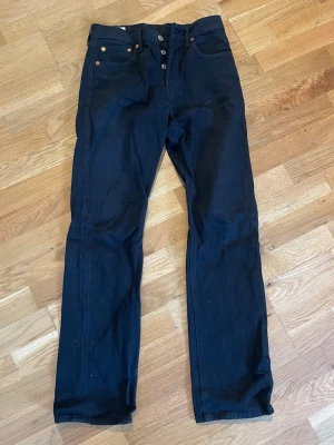 Svarta raka jeans från Levi's - Säljer ett par svarta jeans från Levi's med rak passform och klassisk femficksdesign. Jeansen har knappgylf och detaljer i kopparfärg. Perfekta för dig som gillar en clean och tidlös look.