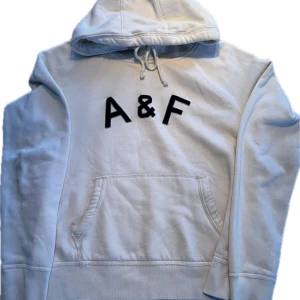Vit hoodie från Abercrombie & Fitch (sällsynt) - Klassisk vit hoodie från Abercrombie & Fitch med stor svart A&F-logga på bröstet. Hoodien har känguruficka, dragsko i huvan och långa ärmar. Perfekt för en chill och avslappnad stil. Riktig stilren. Tyvärr så har den lite smuts på sig därför priset