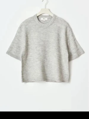 Grå stickad kortärmad tröja - Mjuk och stilren grå stickad tröja med korta ärmar och rund halsringning. Tröjan har en rak passform och ribbstickade kanter vid ärmslut och nederkant. Perfekt för lager-på-lager och enkel att matcha med olika outfits.