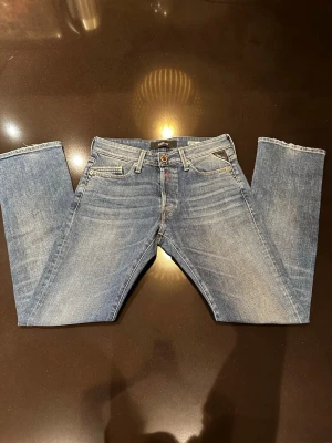 Blå raka jeans från Replay - Säljer ett par klassiska blå jeans från Replay med raka ben och femficksmodell. Jeansen har snygga slitningar och ljus tvätt, samt Replay-lapp i läder bak i midjan. Modell: Waitom. Använda en gång, säljer för att de är för små