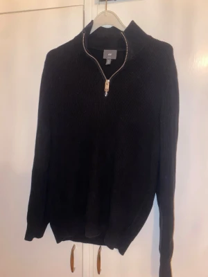 Svart stickad halfzip - Säljer en svart stickad tröja från H&M med halv dragkedja framtill och hög krage. Tröjan har ribbstickad struktur och långa ärmar. Perfekt för lager på lager och enkel att matcha med olika outfits. Storlek XS men passar på mig som oftast bär S.