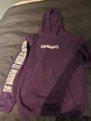 Lila hoodie med tryck och huva - Snygg lila hoodie med huva och magficka. Tryck på bröstet med texten 'Focus Your Energy' och stort tryck längs ena ärmen med texten 'THE WINDOW TO WORLDS BEYOND'. Perfekt för dig som gillar streetwear och unika detaljer.