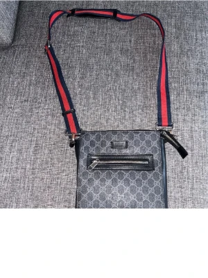 Gucci Messenger bag - Snygg axelväska från Gucci i grått med klassiskt GG-mönster och svart läderdetalj. Väskan har en justerbar axelrem i rött och marinblått samt en praktisk ytterficka med dragkedja. Perfekt för dig som vill ha en trendig och exklusiv accessoar. Fin väska vill ej ha kvar alls säljer billigt första bösta får pris går o diskutera