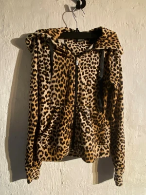 Leopardmönstrad hoodie från Gina Tricot - Säljer en fluffig hoodie från Gina Tricot i storlek XS med leopardmönster. Hoodien har dragkedja framtill, svarta snören i huvan och två stora fickor. Perfekt för dig som vill sticka ut med en djurisk look.