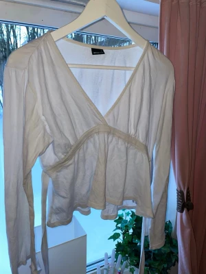 Vit omlottopp från Gina Tricot - Säljer en vit omlottopp från Gina Tricot med långa ärmar och knytband i midjan. Toppen har en djup V-ringning och är tillverkad i ett lätt, mjukt tyg som ger en avslappnad men ändå snygg look. Perfekt att styla med jeans eller kjol.