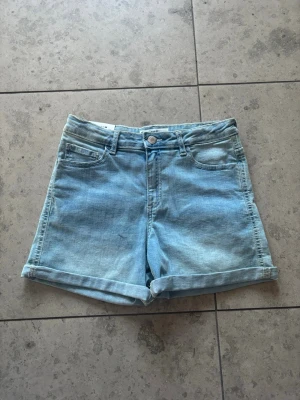 Ljusblå jeansshorts från C Bailey - Säljer ett par ljusblå jeansshorts från C Bailey i klassisk femficksmodell. Shortsen har uppvikta benslut, knapp och dragkedja framtill samt bälteshällor. Perfekta för sommaren och riktigt sköna att bära till t-shirt eller hoodie.