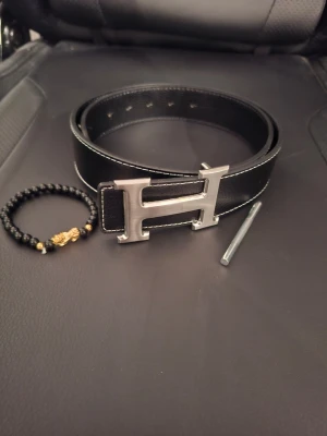 Svart H Bälte - Svart bälte med silvrigt spänne, hål görare och armband ingår, aldrig använd