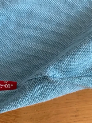 Ljusblå pikétopp från Levi's - Säljer en ljusblå pikétröja från Levi's med klassisk krage och knappslå framtill. Tröjan har korta ärmar och är tillverkad i bomull för en skön och luftig känsla. Perfekt till jeans eller shorts för en avslappnad stil. storleken på denna pikén är 152