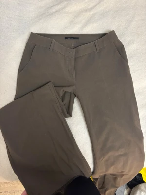 Bruna kostymbyxor från Vero Moda - TALL - Snygga bruna kostymbyxor från Vero Moda med klassisk rak passform och bälteshällor. Byxorna har diskreta fickor och är perfekta för en clean och stilren look. Materialet känns mjukt och har en lätt stretch för extra komfort. Supersnygga o trendiga o passar långa tjejer!