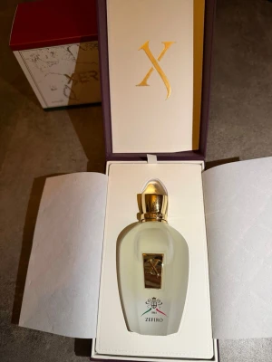 Xerjoff Zefiro parfym 100ml - Lyxig parfym från Xerjoff, modell Zefiro. Flaskan är frostad vit med gulddetaljer och elegant logotyp framtill. Kommer i exklusiv presentförpackning med guldfärgat lock och dekorativt emblem. Perfekt för dig som gillar unika och exklusiva dofter. Kvitto finns ny pris på den är 3000kr