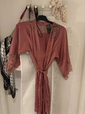 Rosa kimono morgonrock med spets - Snygg rosa kimono morgonrock med breda ärmar och spetsdetaljer vid axlar och ärmslut. Tillverkad i ett glansigt, mjukt material som känns lyxigt mot huden. Denna säljer jag för jag aldrig använt den tyvärr! Den är i storlek XS/S!