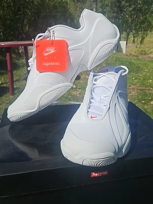 Nike Supreme Air Zoom Flight 98 vita - Säljer ett par vita Nike Air Zoom Flight 98 i samarbete med Supreme. Skorna har en clean design med röda Supreme-detaljer på plösen och tungan samt en orange tag. Ovandelen är i syntetmaterial och mesh, med klassisk Nike-sula och snörning.