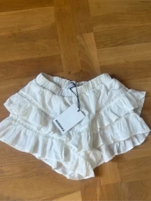 Vita volangshorts från Bershka🌟 - Supersöta vita shorts från Bershka med flera lager volanger och elastisk midja. Lätta och luftiga i ett skönt tyg, perfekta för varma dagar. Snygg detalj med spets längs volangerna.