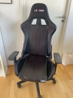 Svart gamingstol från Legend - Säljer en svart gamingstol från Legend med röda detaljer och mönstrad sits. Stolen har justerbara armstöd, hög rygg och hjul för enkel förflyttning. Materialet är konstläder och designen är inspirerad av racingstolar. En del använd och sliten så priset kan diskuteras💕Måste hämtas upp i Helsingborg! Nypris 1650kr