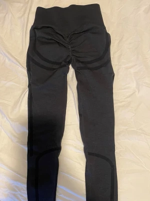 Mörkgråa scrunch leggings från ICIW - Säljer ett par mörkgråa leggings med scrunch. De har mörkare ränder längs benen och runt höfterna för extra form. De är stretchiga och formar kroppen bra.