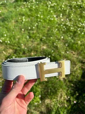 H bälte vit/guld - Tja säljer nu ett helt nytt bälte som är riktigt snyggt om man vill kan man vända på det så kan man ha den svarta, 110cm.                                            Hör av er vid frågor!