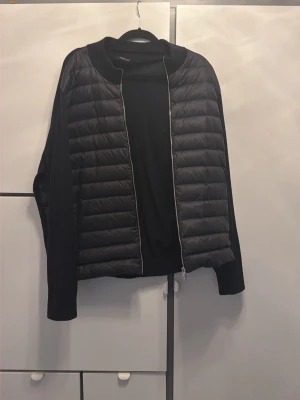 Svart pufferjacka med dragkedja - Snygg svart massimo dutti cardigan med quiltad framsida och släta ärmar. Jackan har en hel dragkedja framtill och en stilren, minimalistisk look. Perfekt för dig som gillar enkel och modern stil.