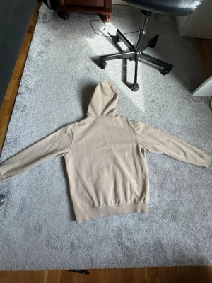 Beige hoodie med ficka framtill - Snygg beige hoodie från Weekday med klassisk känguruficka och dragsko i huvan. Mjuk bomullskänsla och ribbade muddar vid ärmslut och nederkant. Perfekt för en avslappnad och stilren look.