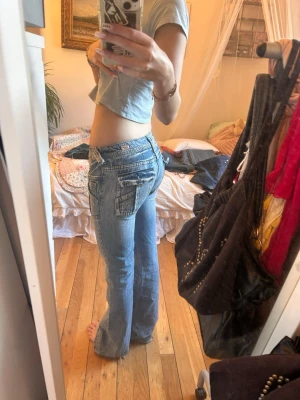 Blå low waist jeans med stora fickor - Säljer ett par ljusblå low waist jeans med breda ben och stora fickor fram och bak. Jeansen har en avslappnad passform och coola slitningar för en trendig look. Perfekta för dig som gillar 00-talsstil och vill ha något bekvämt men ändå snyggt.