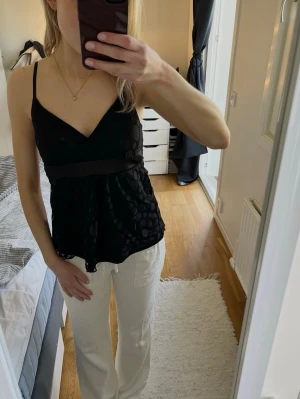 SPETSLINNE - Snygg svart topp från Gina Tricot med tunna axelband och v-ringnign. Toppen har ett brett satinband under bysten och ett prickigt spetslager. Perfekt att styla med jeans eller kjol för fest eller middag! Har använts ett antal gånger och något sliten i sömmarna. 