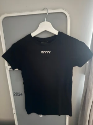 Svart tränings t-shirt från Aim'n - Snygg svart t-shirt från Aim'n med vit logga tryckt på bröstet. Klassisk rund halsringning och korta ärmar. Tillverkad i mjuk bomull som känns skön mot huden. Perfekt för en clean och enkel look.