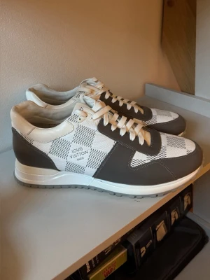 Louis Vuitton gråvita sneakers - Snygga sneakers från Louis Vuitton i grått och vitt med klassiskt rutmönster och tydlig logga på sidan och hälen. Skorna har lågt skaft, vita snören och en robust sula. Materialet är en mix av läder och textil för en exklusiv känsla. Kan också byta men andra skor som till exempel masion margelas skor. Pris kan diskuteras 