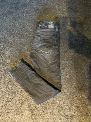 Svarta Replay anbass - Säljer ett par svarta  jeans från Replay med smal passform i modellen Anbass och storlek W30 och L32 jeansen har  klassisk femficksdesign. Jeansen har tydliga sömmar och en snygg tvättad look. Perfekta för dig som gillar stilrena och bekväma jeans.