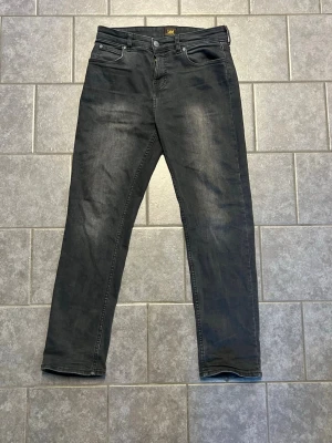 Svarta jeans från Lee - Snygga svarta jeans från Lee med klassisk femficksdesign och raka ben. Jeansen har en lätt tvättad look och är tillverkade i ett mjukt denimtyg som ger en bekväm känsla.perfekt för dig som gillar en stilren outfit!