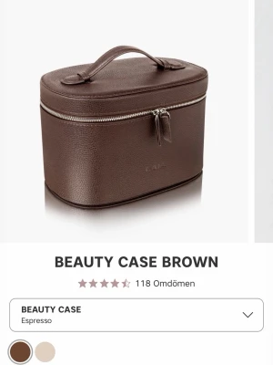 Brun beauty case i läderlook - Snygg och rymlig beauty case i mörkbrun färg från CaiA. Väskan har en stilren oval form, praktiskt handtag upptill och silverfärgad dragkedja. Insidan har smarta fack och avtagbar insats för smidig organisering av smink eller hudvård. Perfekt för att hålla ordning på dina essentials.