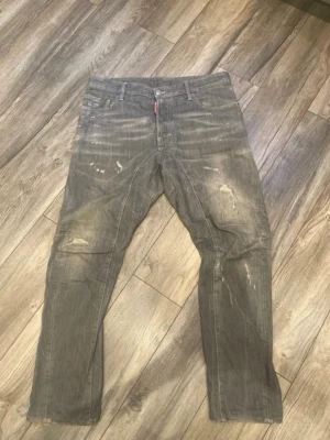 Gråa jeans med slitna detaljer - Säljer ett par gråa jeans med coola slitningar och unika tvättade effekter. Jeansen har raka ben och klassisk femficksdesign. Perfekta för dig som gillar en avslappnad och trendig streetstil.