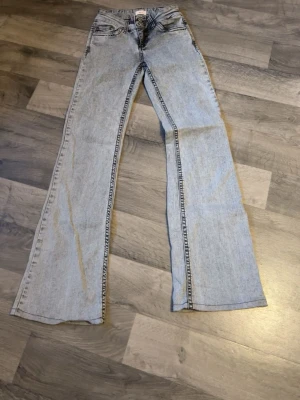 Gråa bootcut jeans med kontrastsömmar - Säljer ett par gråa bootcut jeans med snygga kontrastsömmar och klassiska fem fickor. Baksidan har två fickor med zigzag-detaljer. Jeansen har hög midja och är tillverkade i denim, perfekta för en avslappnad och trendig look.