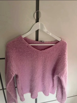 Ljusrosa fluffig stickad tröja - Supermjuk och fluffig ljusrosa stickad tröja från MEET ME THERE. Tröjan har v-ringning och långa ärmar, perfekt för att hålla sig varm och snygg. Materialet är lurvigt och ger en mysig känsla.