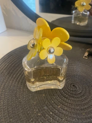 Daisy parfym från Marc Jacobs - Daisy från Marc Jacobs är en ikonisk parfym i en genomskinlig glasflaska med dekorativt lock prytt av stora gula och vita blommor med silvriga detaljer. Flaskan har en söt och lekfull design som verkligen sticker ut på hyllan. Lådan finns inte kvar. Ca 50ml kvar