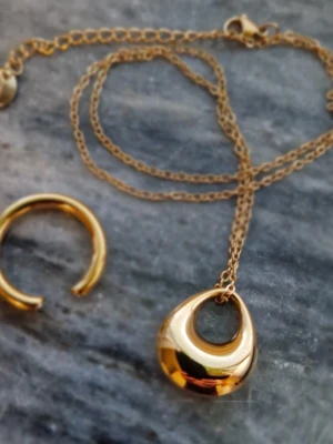 Halsband med hängberlock och ring i guldpläterat stål - Oanvänt smykesset i guldpläterat stål.   Från Guldfynd, serie "GODDESS"  Halsbandskedja 42cm + 5 cm förlängning. Ring, justerbar  Perfekt till studenten!