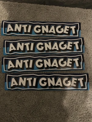Anti Gnaget klistermärken blåsvarta - Fyra rektangulära klistermärken med texten 'ANTI GNAGET' i stora vita bokstäver med svart kontur på blå och svart bakgrund. Perfekt för dig som vill visa ditt stöd för ett specifikt lag eller markera rivalitet.