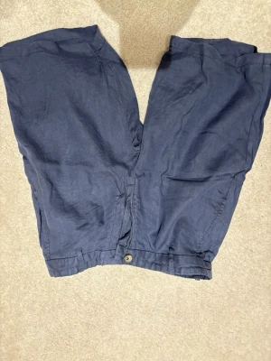 Blå linneshorts från Dressmann | strl M - Snygga mörkblå linneshorts från Dressmann i 100% linne. Byxorna har rak passform, knappstängning och är perfekta för en avslappnad stil. Sköna och luftiga, passar bra till sommaren. Använda endast 1 gång.