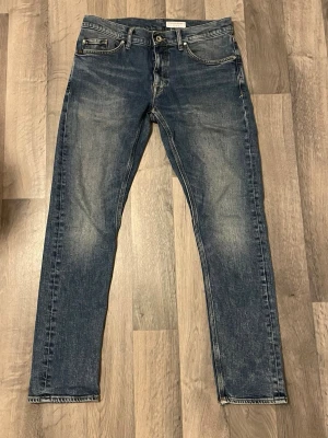 Blå jeans från Tiger of Sweden - Snygga blå jeans från Tiger of Sweden med klassisk femficksdesign och raka ben. Jeansen har en lätt tvättad look med slitningar på låren och är tillverkade i denim. Perfekta för en stilren och avslappnad outfit.