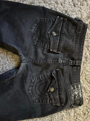 Svarta true Religion jeans - Säljer ett par snygga svarta jeans från true religion med låg midja och utsvängda ben. Modellen heter Joey Low Rise Flare och är i stolek 27w.