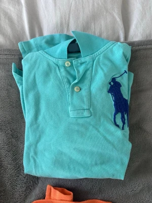 Turkos piké  från Polo Ralph Lauren - S i barnstorlek! Snygg turkos piké från Polo Ralph Lauren med klassisk krage och två knappar framtill. Stor blå broderad logga på bröstet. 