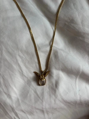 Maria Nilsdotter halsband - Unikt halsband från Maria Nilsdotter  i guldfärgad metall med ett hänge format som änglavingar och en oval, klar sten i mitten.  Denna finns inte länge att köpa någon stans😊