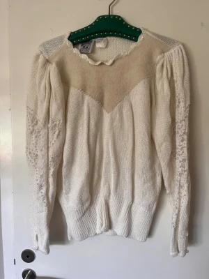 80-tal elegans  - Elegant tröja med otroligt vackra detaljer. En riktig dyrgrip. Spets, pärlor och puffärm. Boutique inköpt i vintage butik i Madrid. 80-tal. Super snyggt till svart pennkjol. Ett måste med oversize.  Beigefärg. *minifläck baktill.  Axel 38cm  Längd 53 cm 