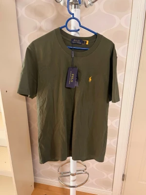 Olivgrön t-shirt från Polo Ralph Lauren - Snygg olivgrön t-shirt från Polo Ralph Lauren med klassisk gul broderad logga på bröstet. T-shirten har rund halsringning och korta ärmar. Tillverkad i mjuk bomull för en skön känsla och stilren look.