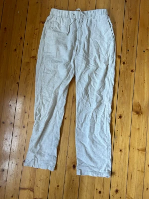 Beiga linnebyxor - Säljer ett par ljusbeige linnebyxor från H&M med avslappnad passform och elastisk midja med dragsko. Byxorna har raka ben och sidofickor, perfekta för en chill och luftig stil. Materialet är 100% linne vilket gör dem svala och sköna. Lappen innuti är avklippt. Storleken är förmodligen S och är 165cm på bilden.