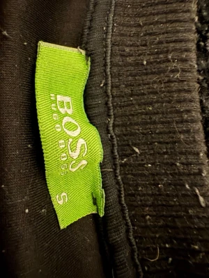 Svart sweatshirt från Hugo Boss - Snygg svart sweatshirt från Hugo Boss med stor logga framtill. Tröjan har rund halsringning, långa ärmar och ribbade muddar vid ärmslut och nederkant. Perfekt för en avslappnad och trendig stil.