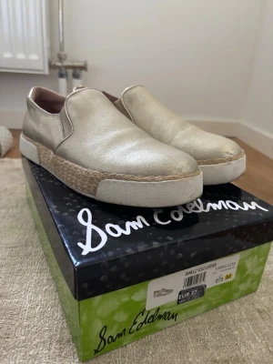 Sam Edelman loafers - Snygga loafers i metallic guld från Sam Edelman. Skorna har en vit gummisula och detaljer i flätad jute runt sulan för en trendig look. Slip-on-modell med rund tå och bekväm passform. Perfekta för dig som vill sticka ut med stil.