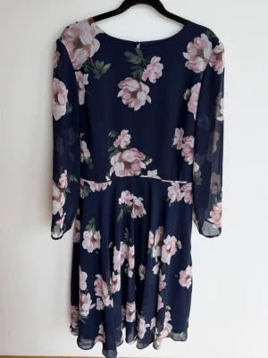 Marinblå blommig klänning - Snygg marinblå klänning med rosa blommor från Hobbs. Klänningen har långärmade, transparenta ärmar och ett flytande, lätt tyg som ger en romantisk känsla. Klänningen har en rund ringning. Perfekt för sommarens alla tillfällen:) Använd en gång. Inga anmärkningar. Säljs i befintligt skick.