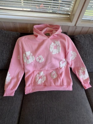 denim tears hoodie - Säljer en rosa hoodie med huva och stora vita kaninmönster över hela tröjan. Hoodien har en klassisk känguruficka framtill och ribbade muddar vid ärmslut och nederkant. Perfekt för dig som gillar gulliga och unika plagg!